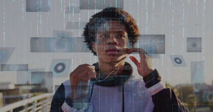 Adjusting wired earphones Black man wearing athletic hoodie on walkway railing with digital overlay