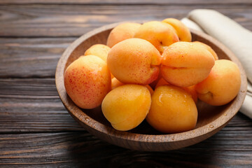 Fresh apricots in bowl on wooden table, closeup