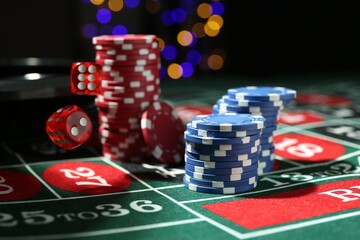 Casino chips and dice falling on roulette table against blurred lights, closeup