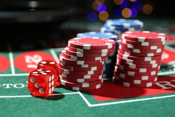 Casino chips and dice on roulette table against blurred lights, closeup