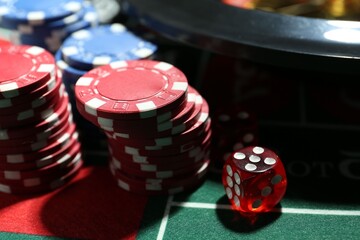 Casino chips, die and roulette wheel on table, closeup