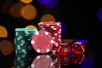 Casino chips and dice on mirror surface against blurred lights, closeup