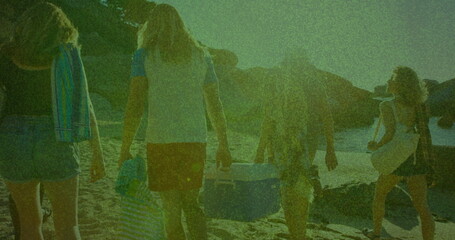 Walking five friends carrying coolers and towels on beach toward rocky shoreline, with straw hat