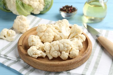 Pieces of cauliflower, peppercorns, oil and knife on light blue wooden table, closeup