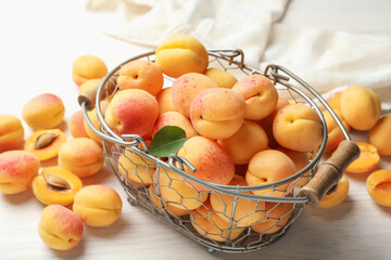 Fresh ripe apricots in metal basket on white wooden table, closeup