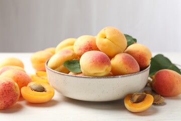 Fresh ripe apricots in bowl and green leaves on white table, closeup