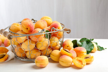 Fresh ripe apricots in metal basket and green leaves on white wooden table