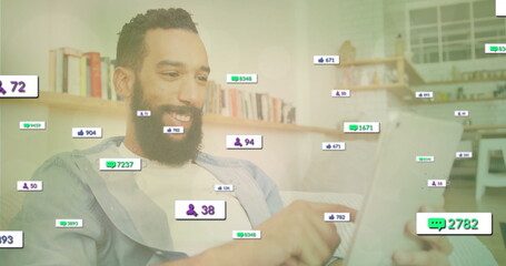 Scrolling bearded man holding tablet on couch in modern living room, with floating reaction icons
