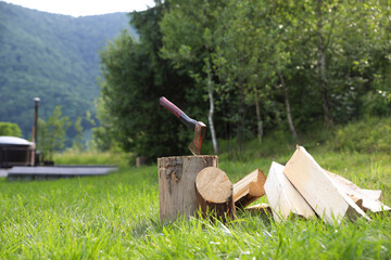 Metal axe, chopped firewood and wooden log on green grass outdoors. Space for text