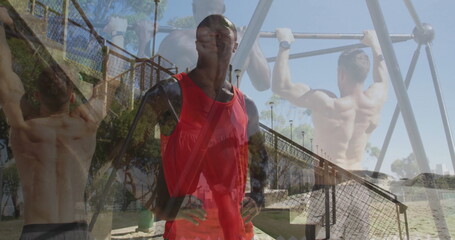 Man in red top, black sleeves with crossbody strap supervising pull-ups on beach, with metal bars