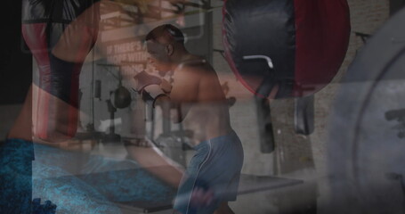 Showing adult woman raising gloves and shirtless man punching bag at boxing gym, with weight bench