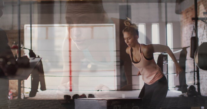 Jumping athlete performing box jump at boxing gym, with plyometric box, ring ropes and heavy bag
