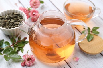 Tasty rose tea, flowers and leaves on white wooden table, closeup