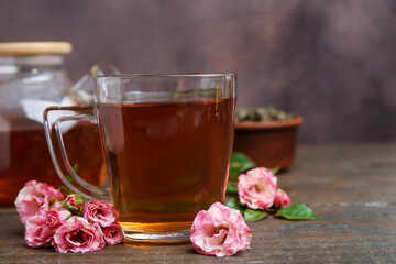 Tasty rose tea in glass cup and flowers on wooden table against brown background, closeup