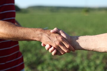 Farmers shaking hands in field outdoors, closeup