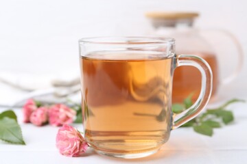 Aromatic tea in glass cup, roses and green leaves on white table, closeup