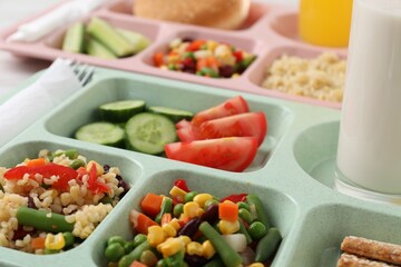 Plastic trays with tasty food, milk and orange juice on table, closeup. School lunch