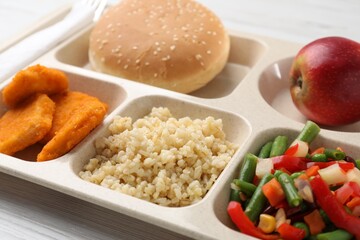 Plastic tray with tasty food on light wooden table, closeup. School lunch