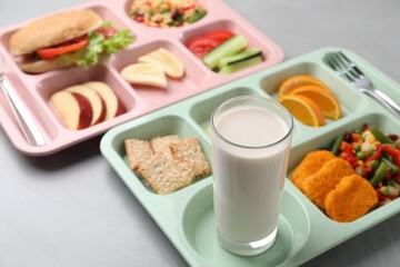 Plastic trays with tasty food and milk on grey table, closeup. School lunch