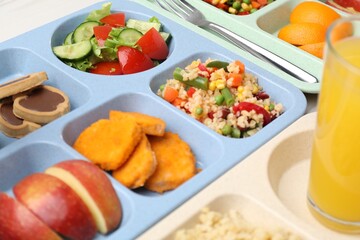 Plastic trays with tasty food and orange juice on table, closeup. School lunch
