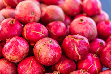 A close-up of a a vibrant red pomegranate from a neatly arranged fruit display at an outdoor farmers market.