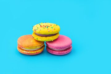 Three brightly colored stacked macarons on blue background. Mixed of colorful macaroni or pasta cake. Tasty and colorful french macarons. Culinary, cooking concept, styling food.