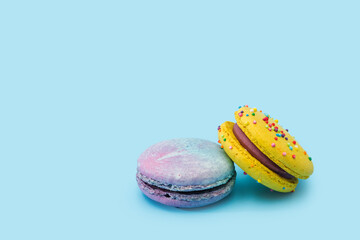 Sweet colorful macarons isolated on light blue background. Tasty colorful macaroons. Two multi-colored blue and yellow macaroons. French pastry made from egg whites. Culinary and cooking concept.