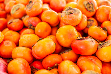 A vibrant display of fresh persimmon fruit arranged neatly for sale at a farmers market, highlighting seasonal produce and tactile interaction with food.