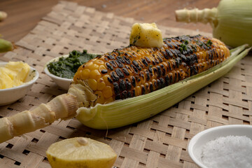 Grilled corn cobs on vintage wood background with lemon, salt, and green chutney or thecha
