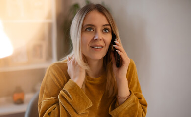 Young woman in mustard sweater talking on smartphone, looking slightly upward with an attentive...