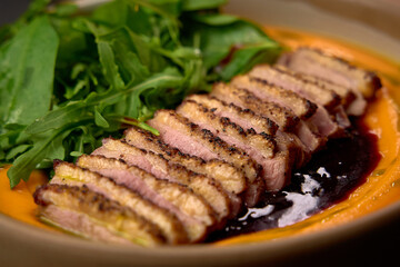 Deliciously Plated Sliced Duck Breast Served on a Bed of Vibrant Carrot Puree with Fresh Greens for a Harmonious Culinary Experience