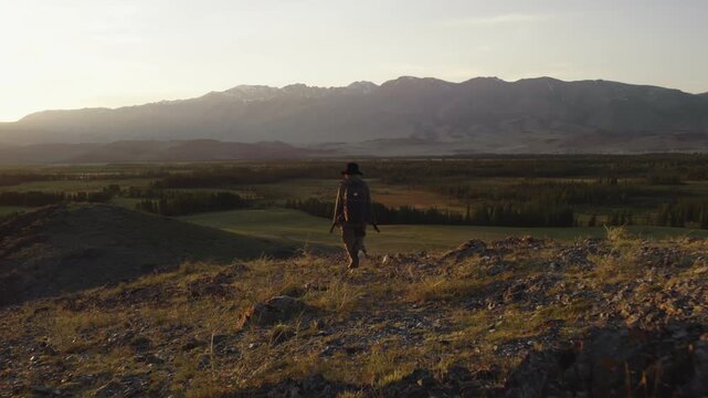 Girl hiker with backpack standing on top of mount enjoying beautiful view of mountain valley and ridge at sunset. Concept of adventure, loneliness, goal achievement, contemplation