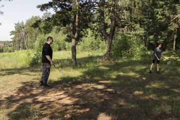 Father and daughter playing badminton in a sunny forest clearing, surrounded by green trees and grass, enjoying outdoor recreation and quality family time in nature.