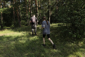 Father and daughter walking slowly through sunlit forest, scanning the ground while foraging for wild mushrooms, enjoying quiet bonding and nature exploration.