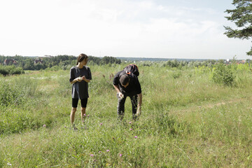 Man and teenage girl exploring grassy field on summer hike, surrounded by blooming wildflowers, symbol of nature appreciation, slow living, mindfulness, and outdoor connection.