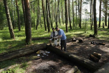 Man and teenage girl cleaning up picnic area in woods, holding biodegradable bags, representing eco-conscious parenting, sustainable habits passed from one generation to the next.
