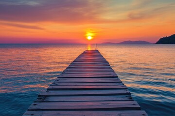Obraz premium Wooden pier extending into a calm sea at sunset. Vibrant colors of orange, pink, and purple paint the sky