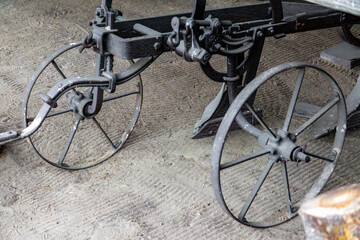 Obraz premium Antique metal plow with iron wheels displayed in a farm building. Old agricultural tool from the pre-mechanized farming era.