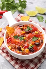Tasty chili con carne in bowl and nachos on grey textured table, closeup