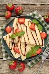 Tasty crepes with strawberries, chocolate sauce and mint on wooden table, flat lay