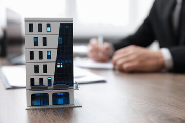 Real estate agent working at desk in office, focus on house model