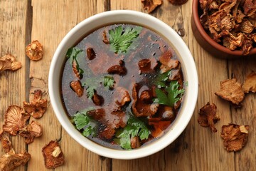 Tasty soup with mushrooms and parsley in bowl on wooden table, flat lay