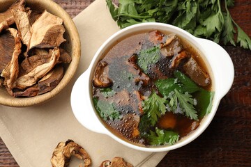 Tasty soup with mushrooms and parsley in bowl on wooden table, flat lay