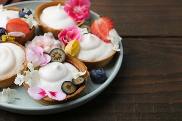 Delicious dessert. Tartlets with cream, berries and flowers on wooden table, closeup. Space for text