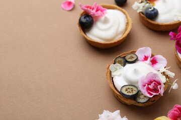 Delicious dessert. Tartlets with cream, berries and flowers on light brown background, closeup....