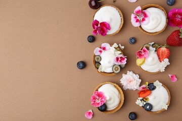 Delicious dessert. Tartlets with cream, berries and flowers on light brown background, flat lay. Space for text
