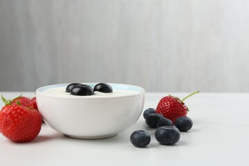 Tasty yoghurt with blueberries and strawberries in bowl on white marble table, closeup. Space for text