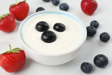 Tasty yoghurt with blueberries and strawberries in bowl on white table, closeup