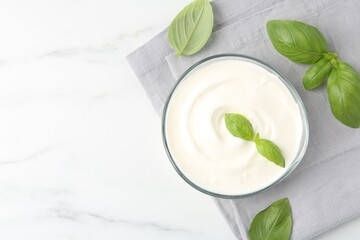 Tasty yoghurt with basil in bowl on white marble table, flat lay. Space for text