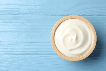 Tasty yoghurt in bowl on light blue wooden table, top view. Space for text